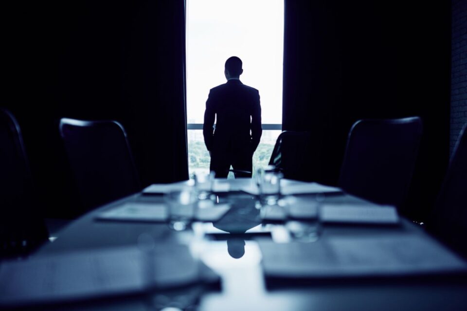 man alone in a meeting room staring out a window