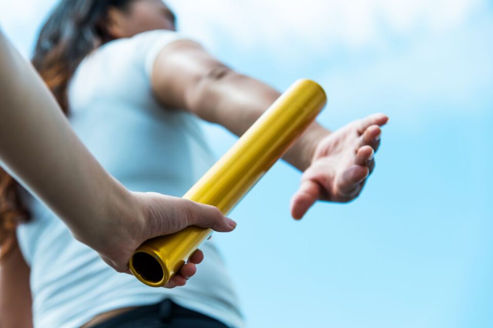 One person passing the baton to another to signify business succession.