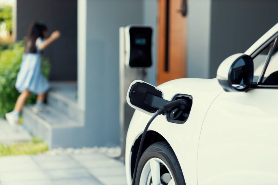 Focus EV car recharging at home charging station for with blur girl in backdrop.