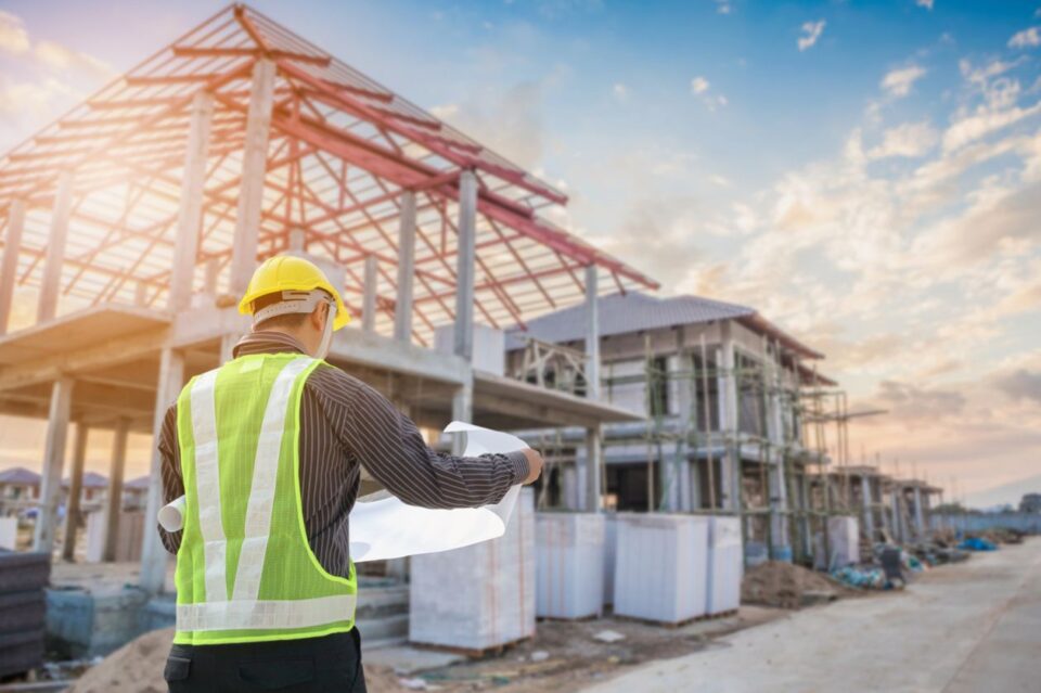 Construction worker looking at plans outside next to a commercial building under construction